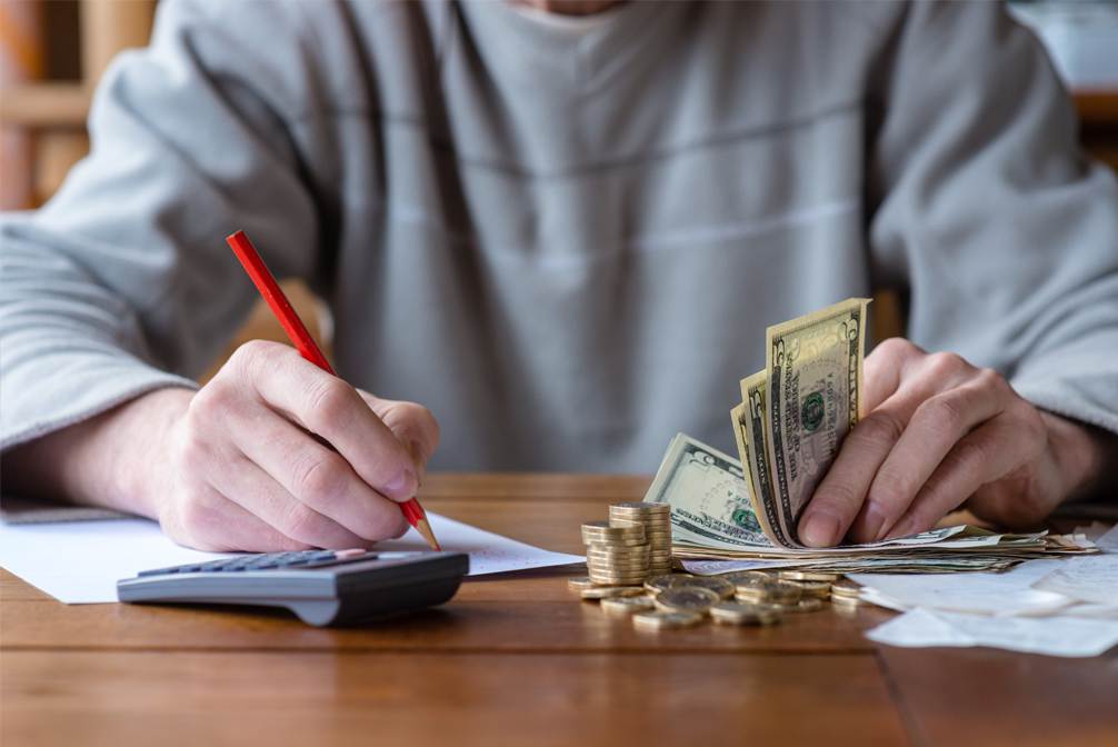 Man seated at table with calculator and money, working on budget