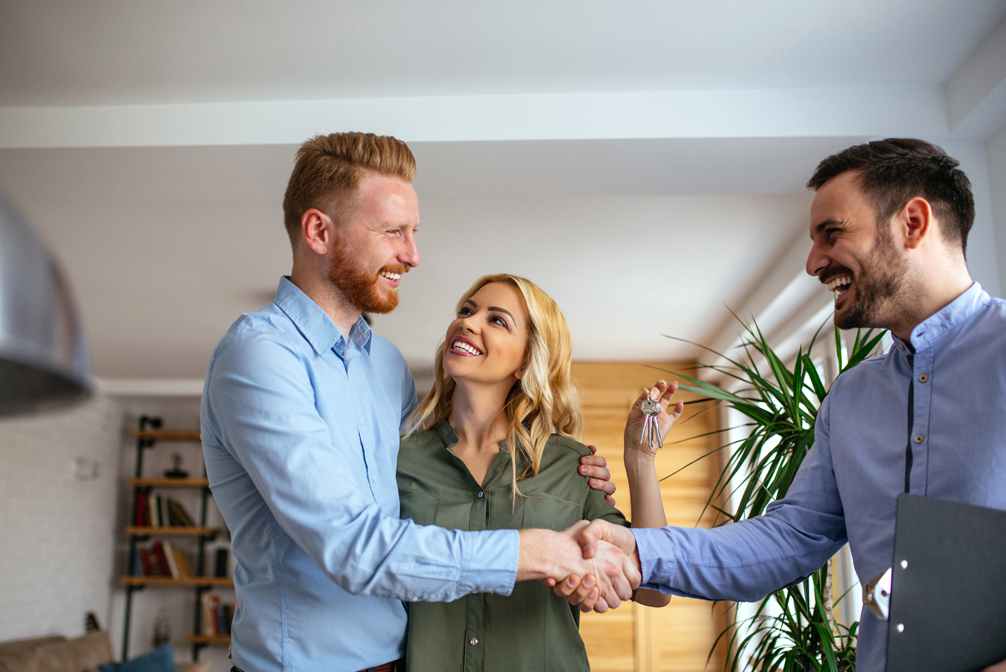 Happy couple new homeowners shaking hands with real estate agent