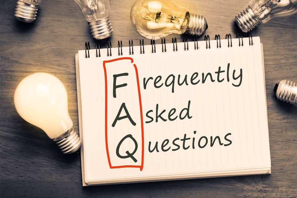 Frequently Asked Questions written on a notebok on a table next to a lightbulb