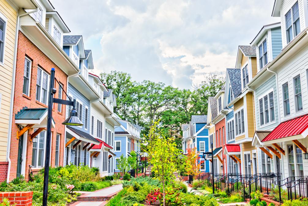 Row of colorful, red, yellow, blue, white, green painted residential townhouses, homes, houses with brick patio gardens in summer