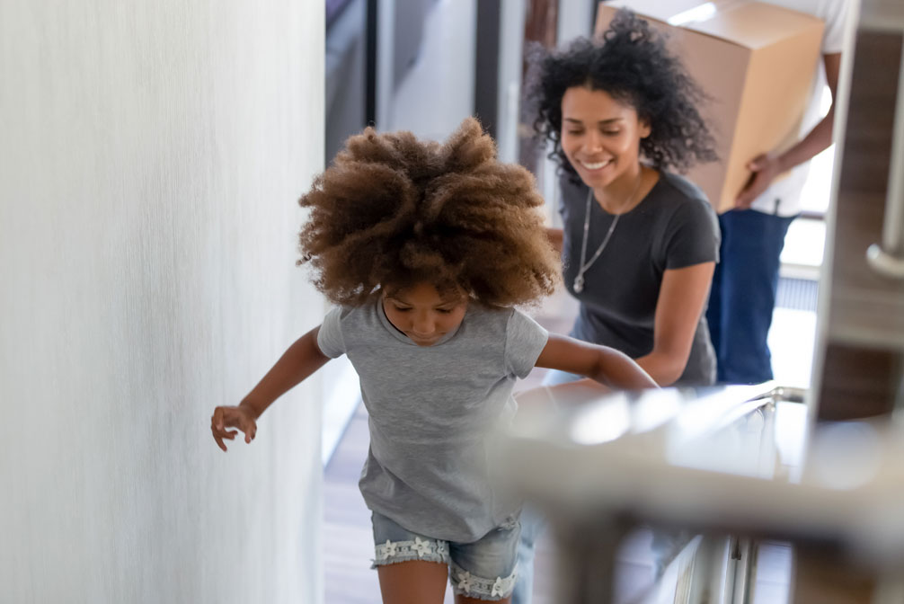 Happy mixed-race girl running up the stairs in new home with parents following behind