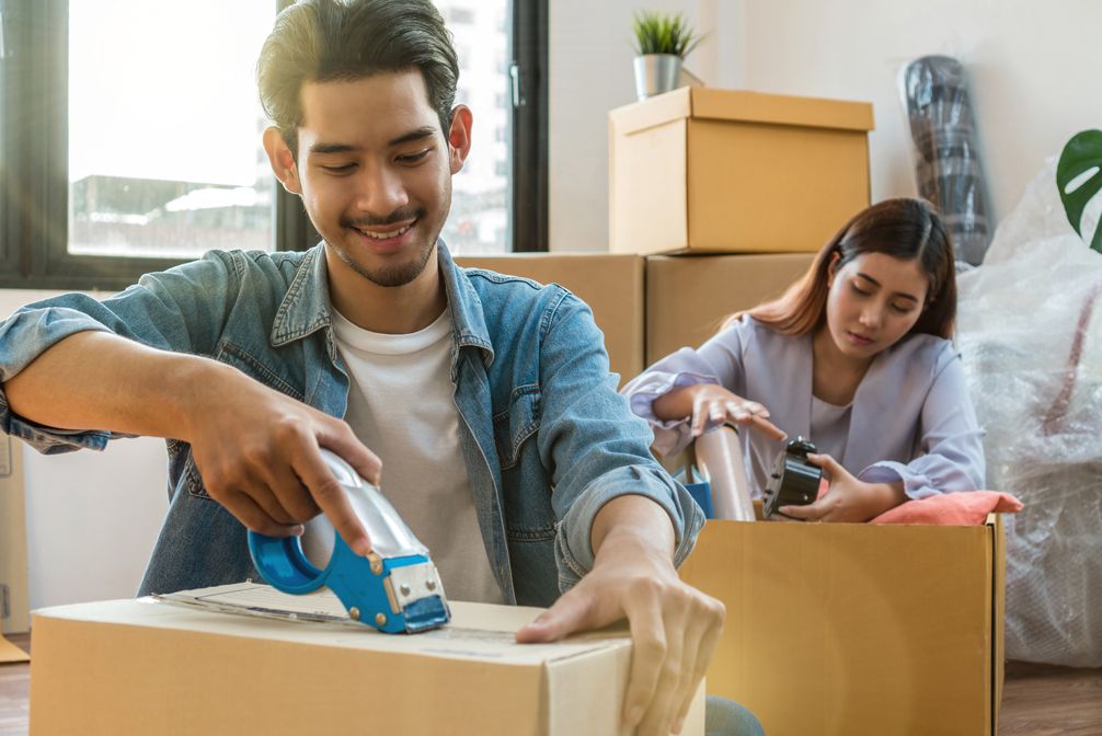 Asian couple home owners packing big cardboard box for moving in new house